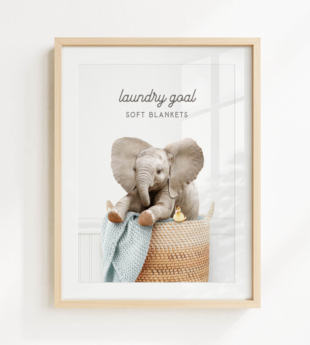 A framed image of an elephant sitting in a woven basket, with a blanket draped over its back.