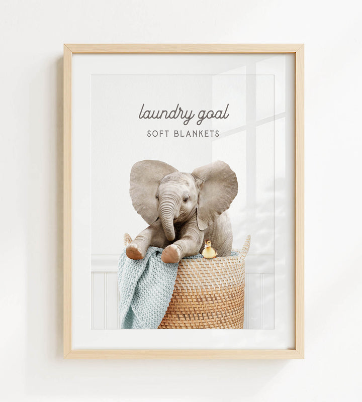 A framed image of an elephant sitting in a woven basket, with a blanket draped over its back.