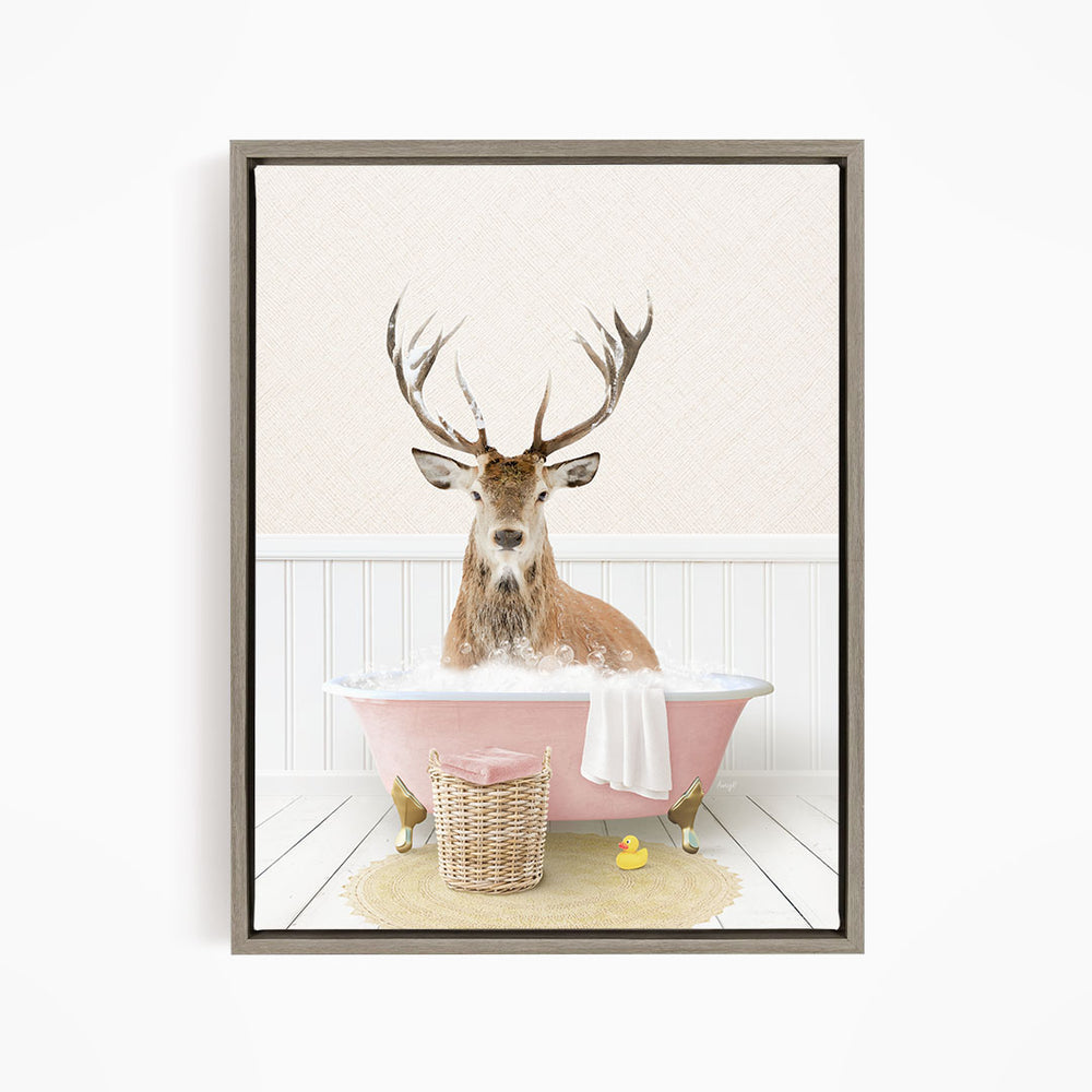 A deer with large antlers is sitting in a pink bathtub filled with bubbles, surrounded by a yellow rubber duck and a basket.