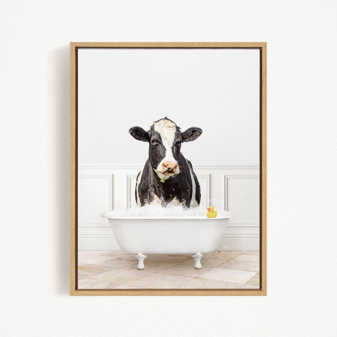 A black and white cow is standing in a white bathtub filled with water, with a rubber duck floating in the water.