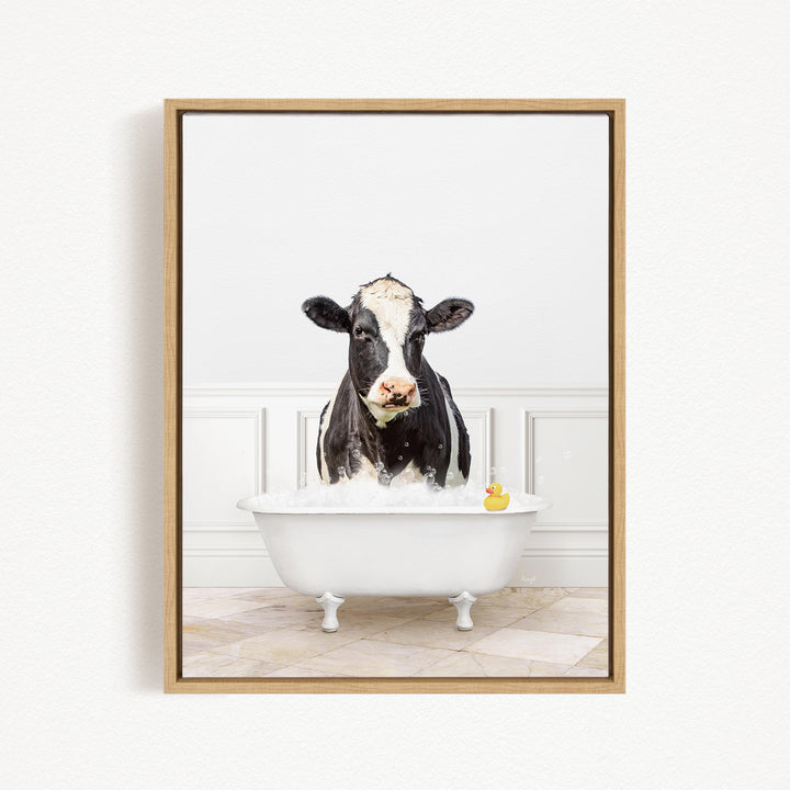 A black and white cow is standing in a white bathtub filled with water, with a rubber duck floating in the water.