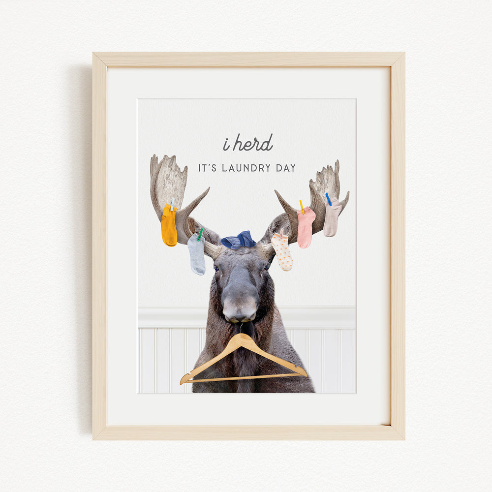 A framed image depicting a moose with a laundry basket hanging from its antlers, accompanied by the text "It's laundry day"