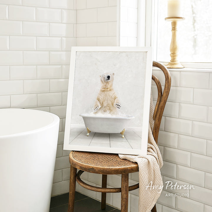 A framed image of a polar bear sitting in a bathtub is displayed on a wooden chair in a bathroom setting.