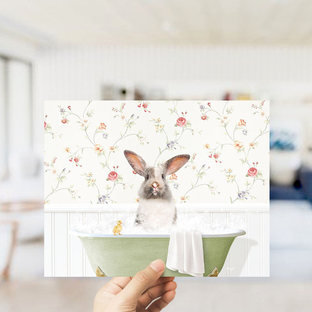 A hand holding a framed print of a rabbit sitting in a bathtub filled with bubbles, surrounded by a floral wallpaper.