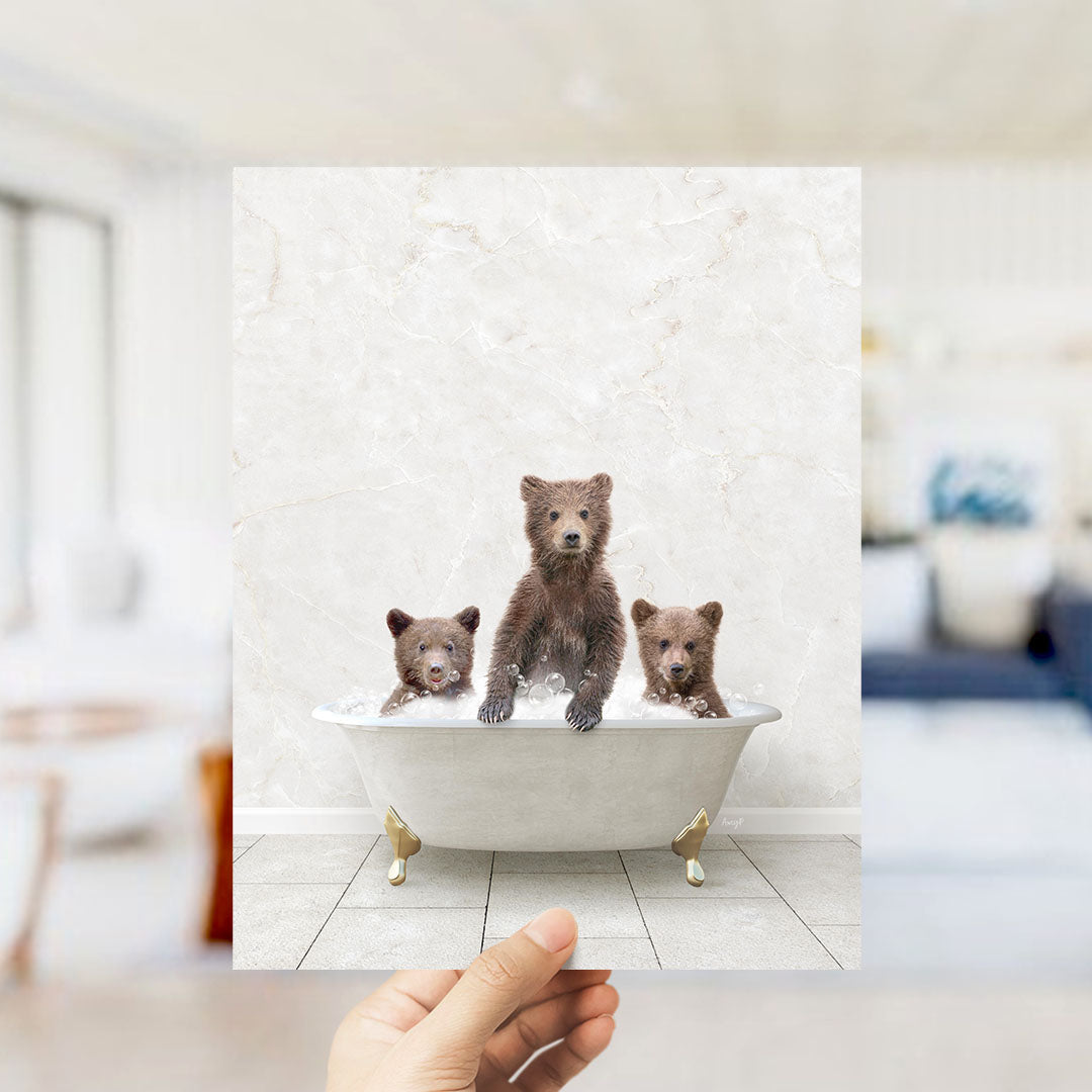 A hand holds up a framed image of three adorable brown bears sitting in a white bathtub, with one bear sitting on the edge of the tub and the other two bears sitting inside the tub.
