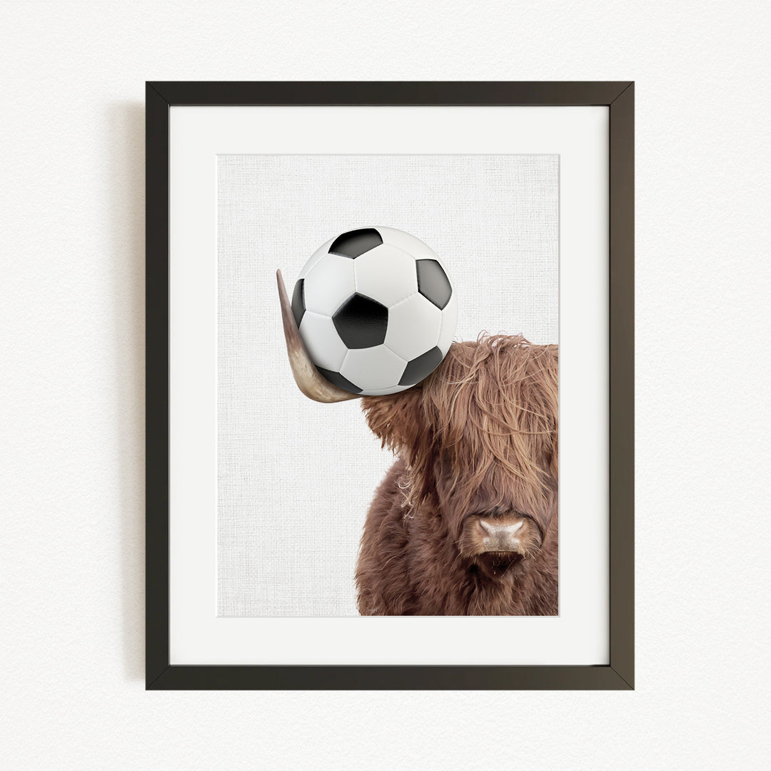 A framed image of a brown cow with a soccer ball on its head.