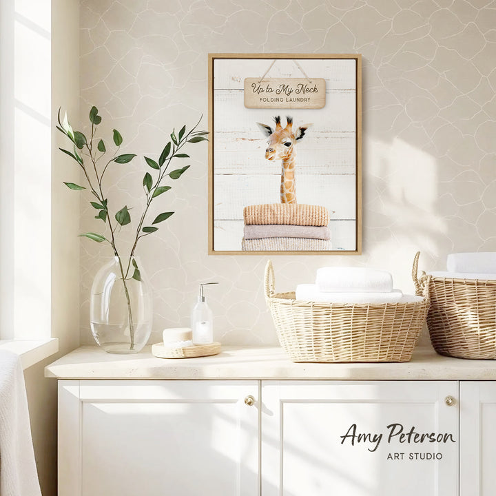 a framed picture of a giraffe on a wall, with a wicker basket and a vase of leaves on a counter below it.