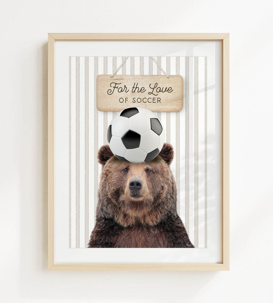 A framed image of a brown bear with a soccer ball on its head, accompanied by a wooden sign that reads "For the Love of Soccer".