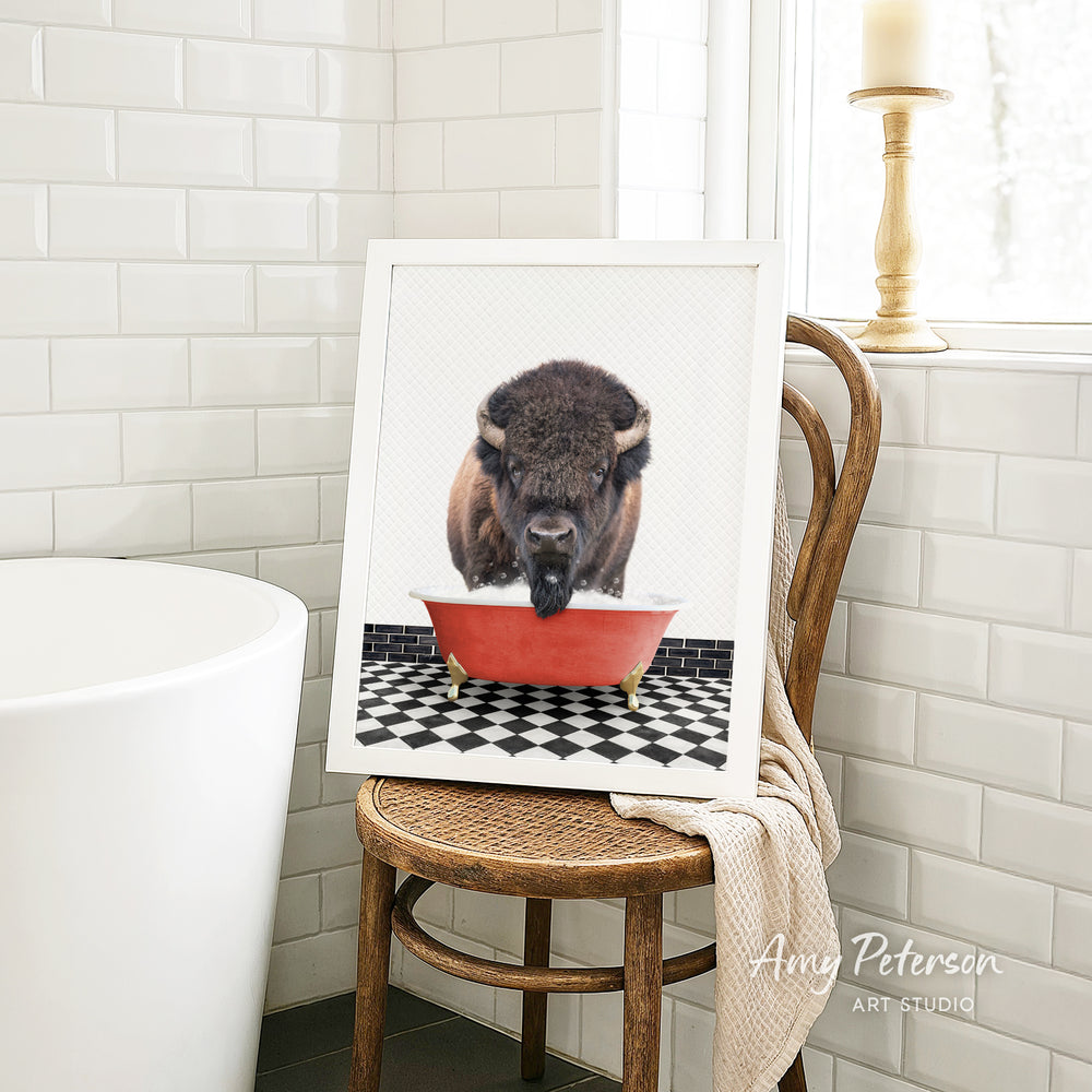 A framed image of a bison sitting in a red bathtub, with a black and white checkered floor in the background.