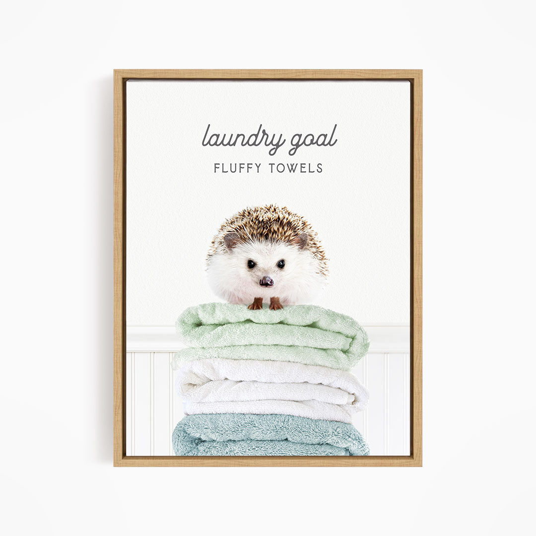 A framed image of a hedgehog sitting atop a stack of fluffy towels, with the text "laundry goal FLUFFY TOWELS" written above it.