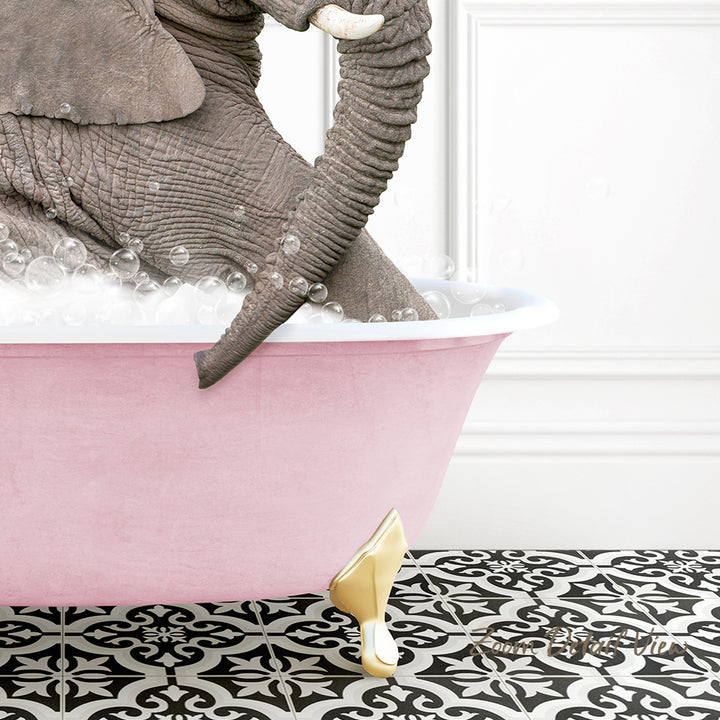A large gray elephant is sitting in a pink bathtub filled with bubbles, with a gold-colored bathtub faucet and gold-colored bathtub feet visible.