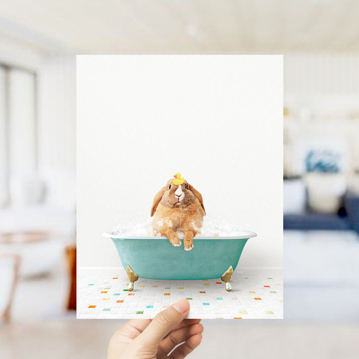 A hand holds up a photograph of a brown rabbit sitting in a green bathtub filled with bubbles, surrounded by a colorful tiled floor.