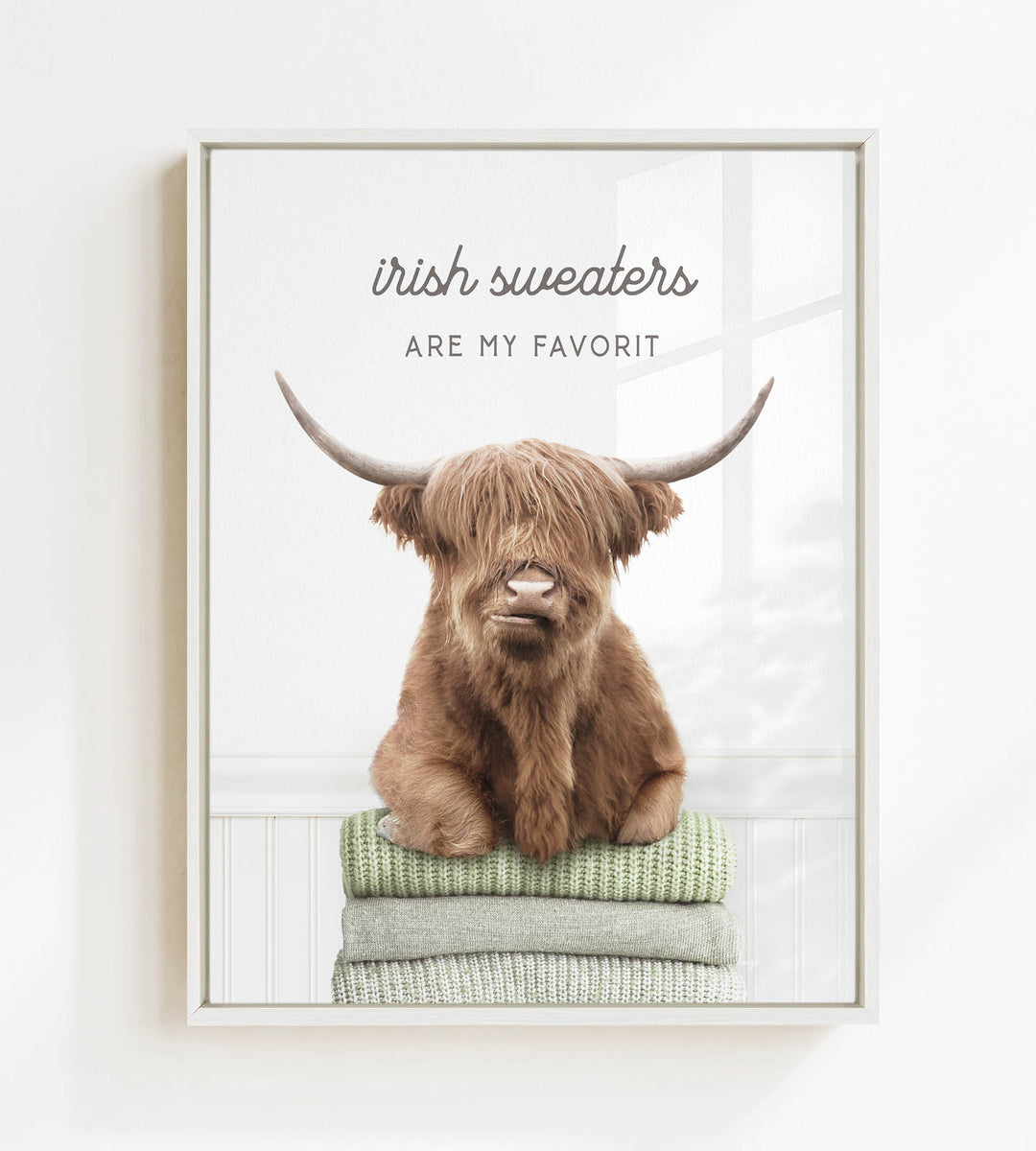 a brown cow with long horns sitting on a stack of green and white sweaters.