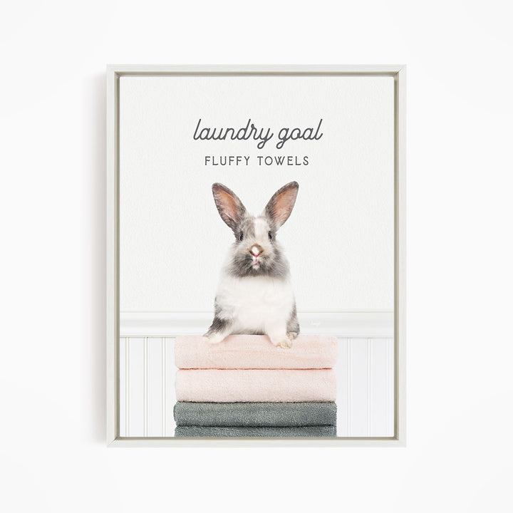 A fluffy white rabbit sitting on a stack of towels, with the text "laundry goal FLUFFY TOWELS" displayed above the rabbit.