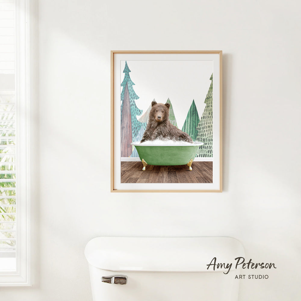 A framed image of a bear sitting in a green bathtub, surrounded by pine trees, is hanging on a white wall.