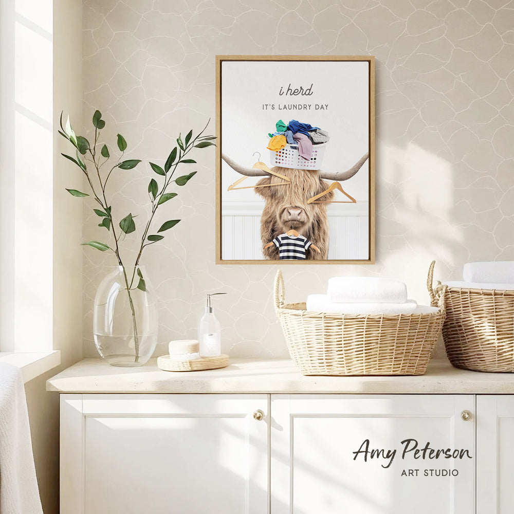 a framed poster of a cow with clothes on its horns, hanging on a wall above a white cabinet with baskets.
