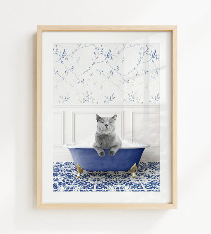 A gray cat sitting in a blue bathtub filled with bubbles, with a patterned tile floor and a floral wallpaper in the background.