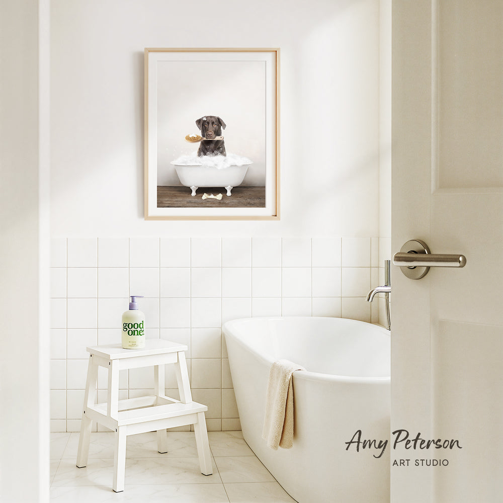 A framed image of a dog sitting in a bathtub, with a towel draped over the side of the tub, is displayed on the wall above a white bathtub in a clean, white-tiled bathroom.