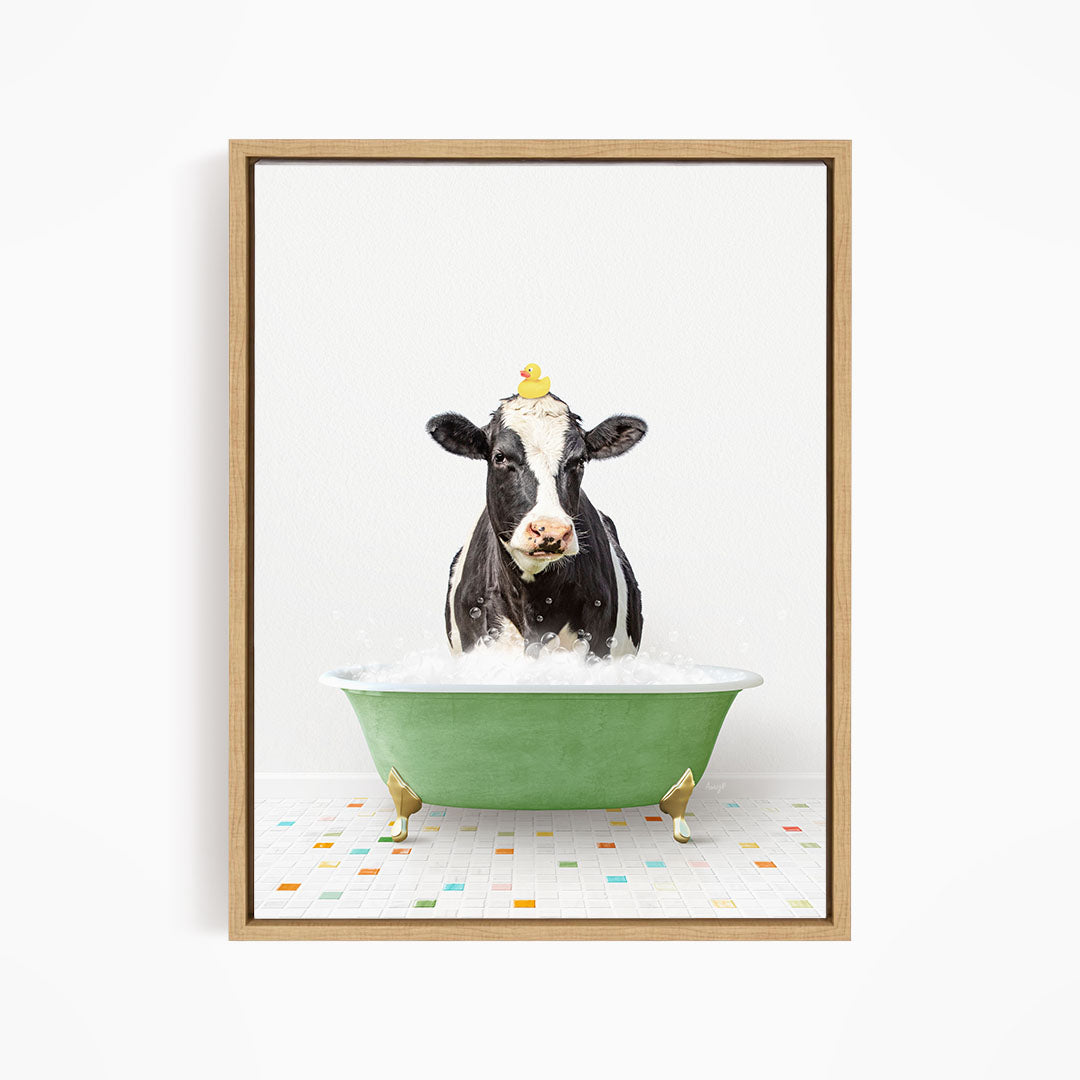 A black and white cow is sitting in a green bathtub filled with water, with a yellow rubber duck perched on its head.