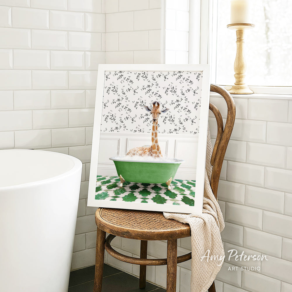 A framed image of a giraffe sitting in a green bathtub, surrounded by a floral pattern, is displayed on a wooden chair in a bathroom setting.