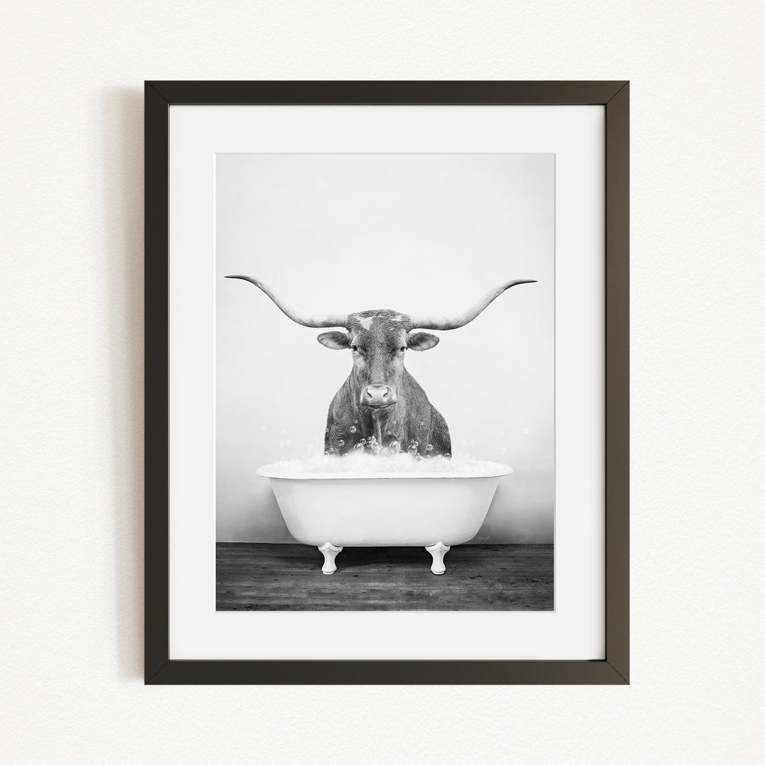 A black and white photograph of a bull with long horns standing in a bathtub filled with water.