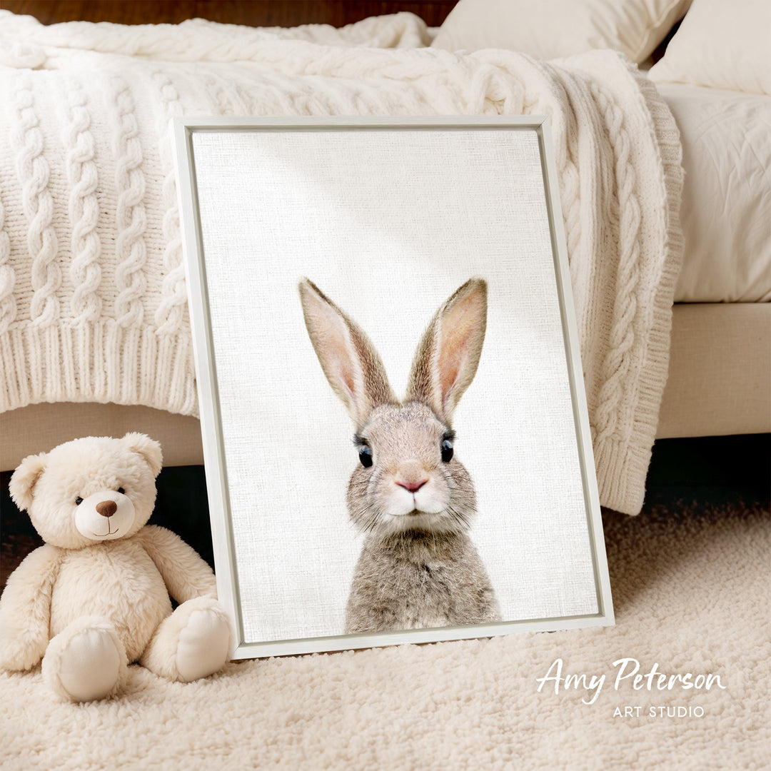 A framed image of a rabbit is displayed on a white bedspread, accompanied by a teddy bear on the floor.