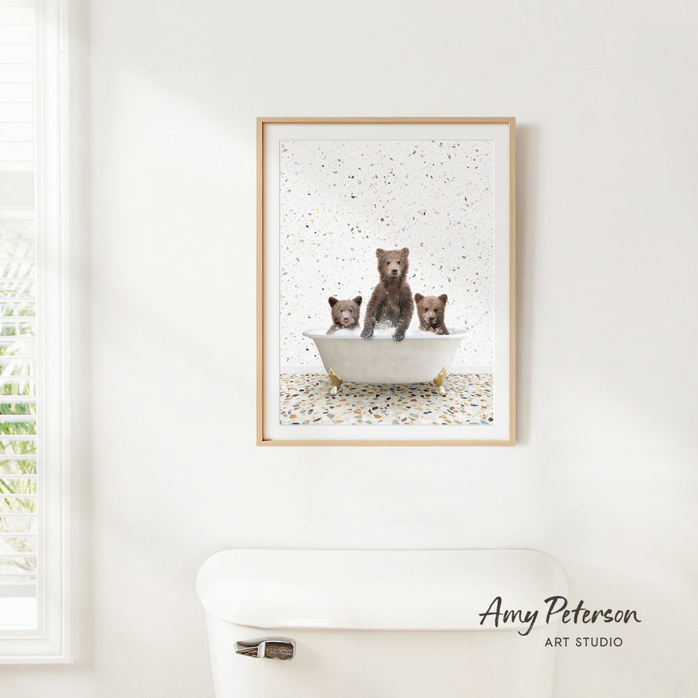 A framed print of three bears sitting in a bathtub is hanging on a white wall.