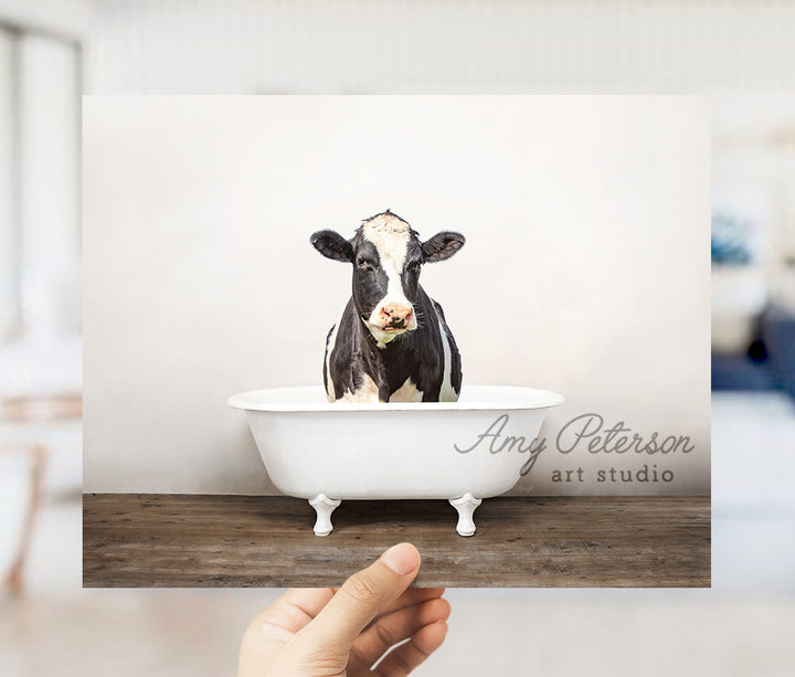 a hand holding up a card with a picture of a cow in a bathtub