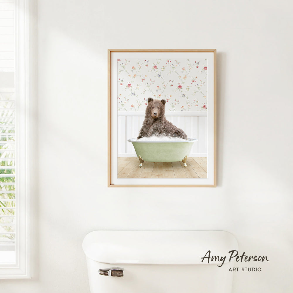 A framed image of a brown bear sitting in a green bathtub, with a floral pattern on the wall behind it.