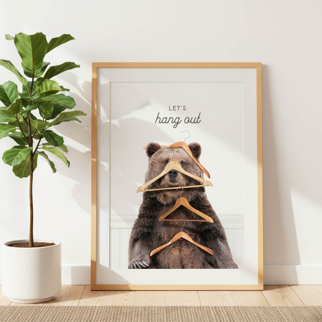 A framed image of a bear sitting on a pile of hanging clothes, with the text "Let's hang out" written above it.