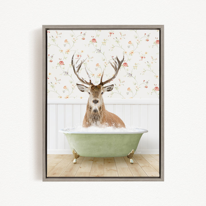 A deer with large antlers is sitting in a green bathtub filled with water, surrounded by a floral wallpaper.