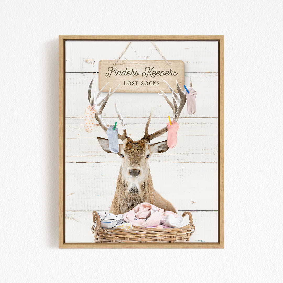 A deer with antlers is sitting in a wicker basket filled with socks, with a sign above that reads "Finders Keepers Lost Socks".