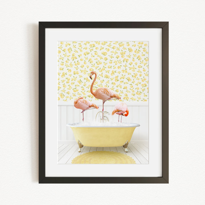 A framed image depicting three pink flamingos standing in a yellow bathtub, with a yellow floral wallpaper in the background.
