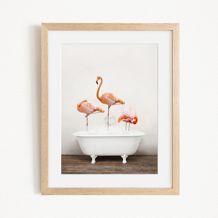 A framed image depicting three flamingos standing in a white bathtub filled with water.