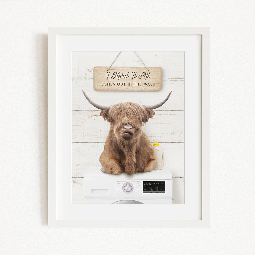 A framed image of a Highland cow with large horns sitting on a washing machine, with a sign above that says "I herd it all comes out in the wash".