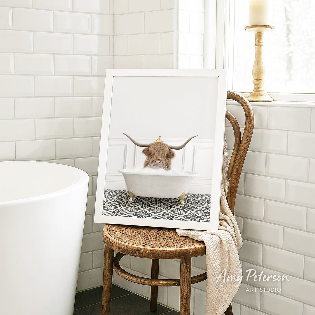 A framed image of a cow with horns sitting in a bathtub, surrounded by a patterned rug, is displayed on a wooden chair in a bathroom setting.