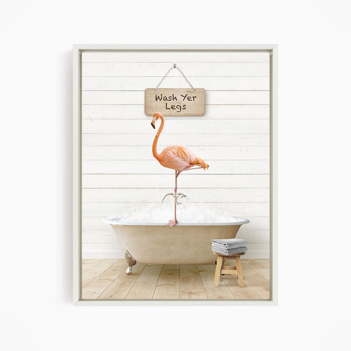 A framed image depicting a pink flamingo standing in a bathtub, with a sign above it that reads "Wash Your Legs".