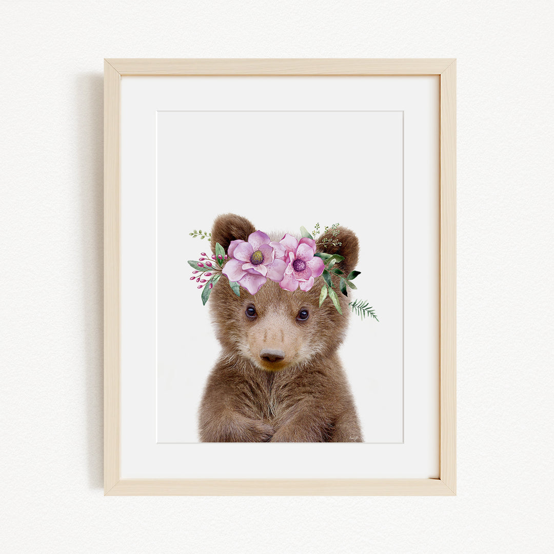 A cute brown bear wearing a floral crown on its head, with its eyes looking directly at the camera.