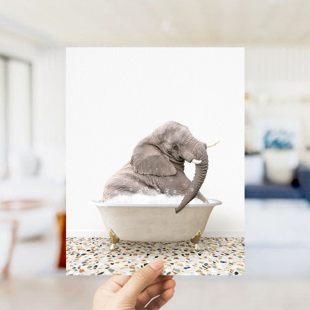 A gray elephant sitting in a white bathtub filled with bubbles, with a hand holding the image up to the viewer.