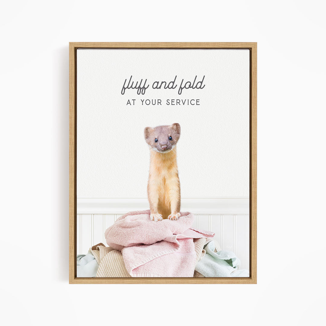 A small brown cat sitting on a pile of clothes, with the text "fluff and fold at your service" written above the cat.
