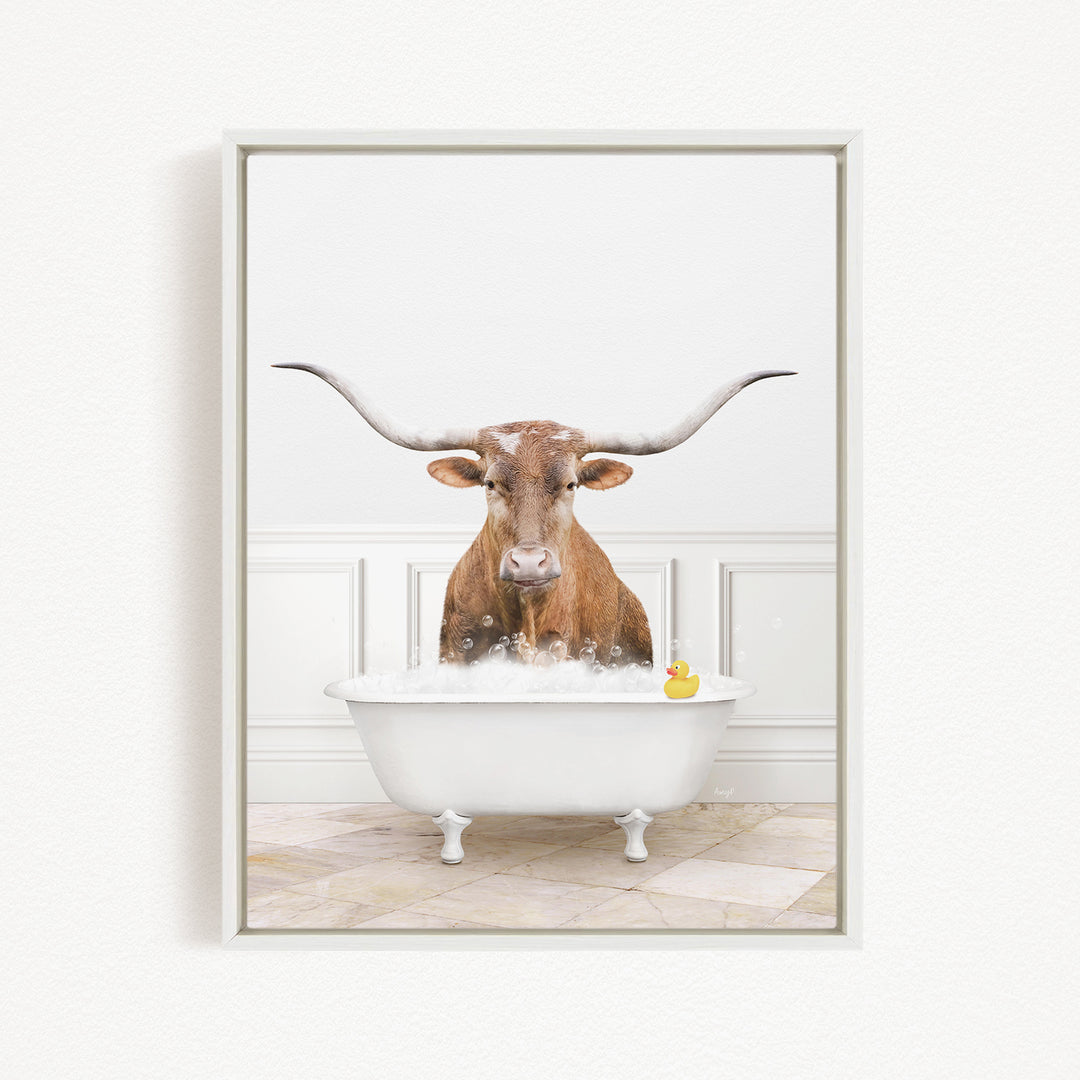 A brown cow with long horns is sitting in a white bathtub filled with water, with a yellow rubber duck floating in the water.