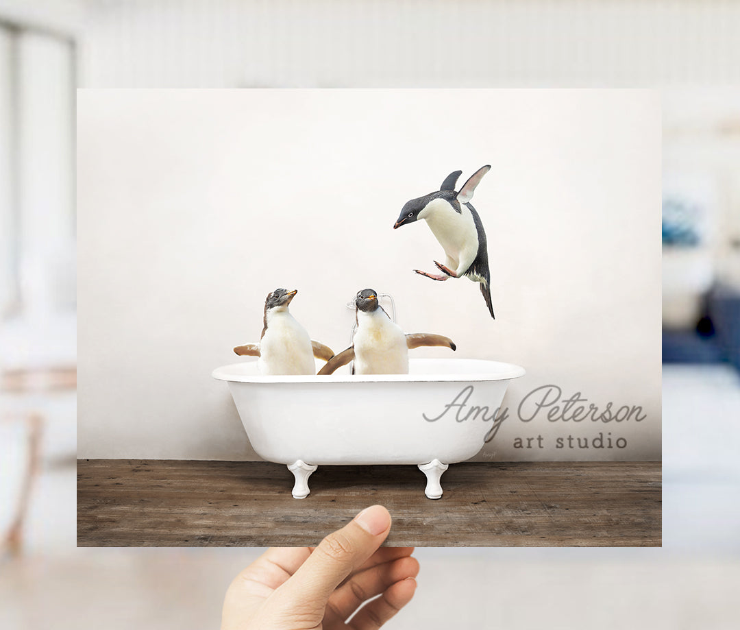 a hand holding a card with three penguins in a bathtub