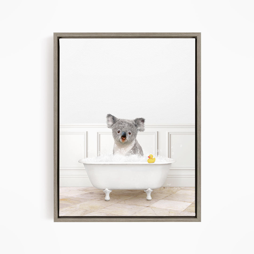 A koala bear sitting in a white bathtub filled with bubbles, with a rubber duck floating in the water.