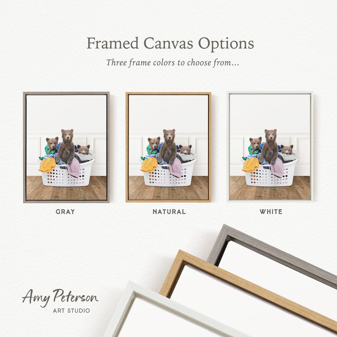 three framed canvas options, each featuring a brown bear sitting in a basket filled with laundry. The options include a gray frame, a natural frame, and a white frame.