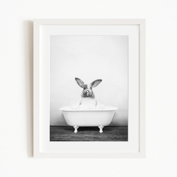 A black and white photograph of a rabbit sitting in a white bathtub filled with water.
