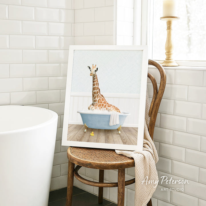 A framed image of a giraffe sitting in a bathtub, with a towel draped over the side of the tub.