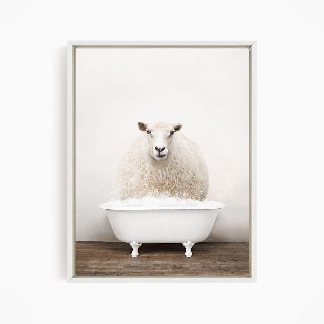 A fluffy white sheep sits in a white bathtub filled with bubbles, looking directly at the camera.