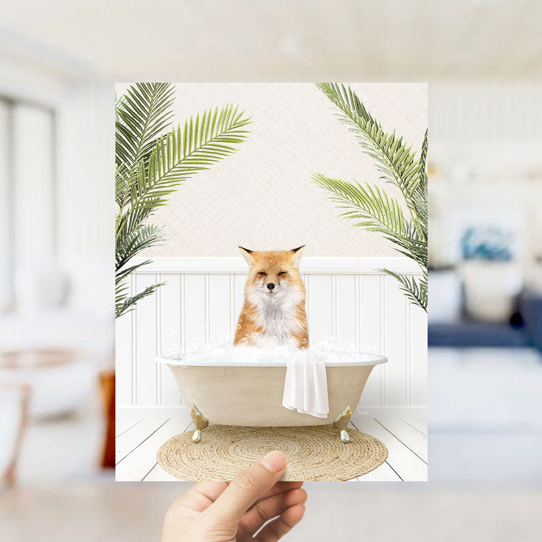 A hand holds up a framed image of a fox sitting in a bathtub filled with bubbles, surrounded by green palm leaves.