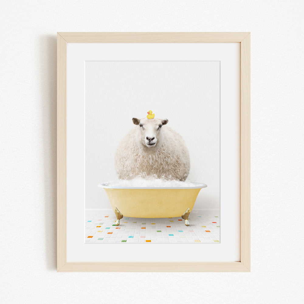 A fluffy white sheep sits in a yellow bathtub filled with bubbles, with a yellow rubber duck perched on its head.