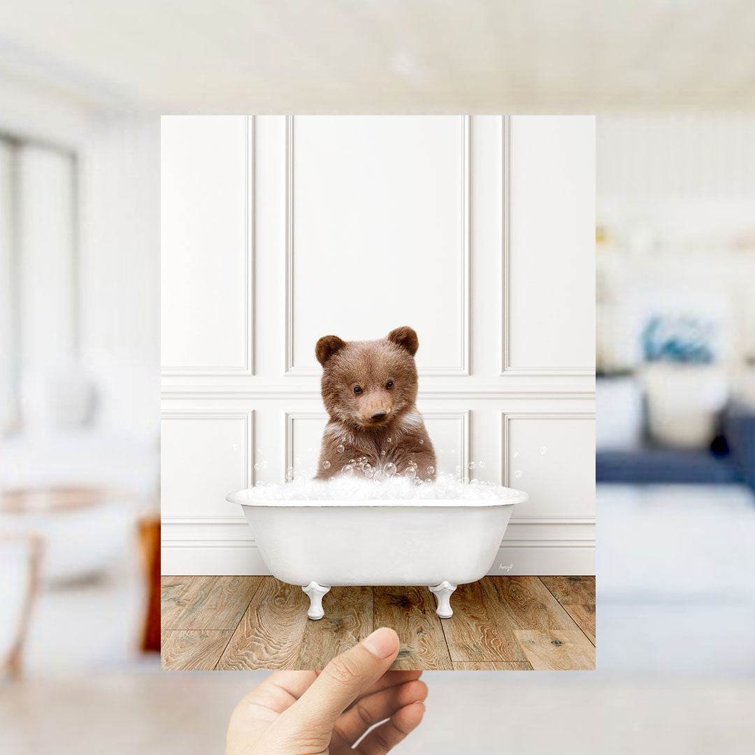 A brown bear sitting in a white bathtub filled with bubbles, with a blurred background suggesting a bathroom setting.